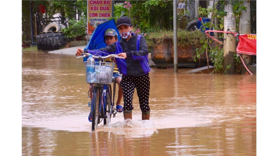 A woman pushes a child on a bicycle through a flooded street in Quang Tri.