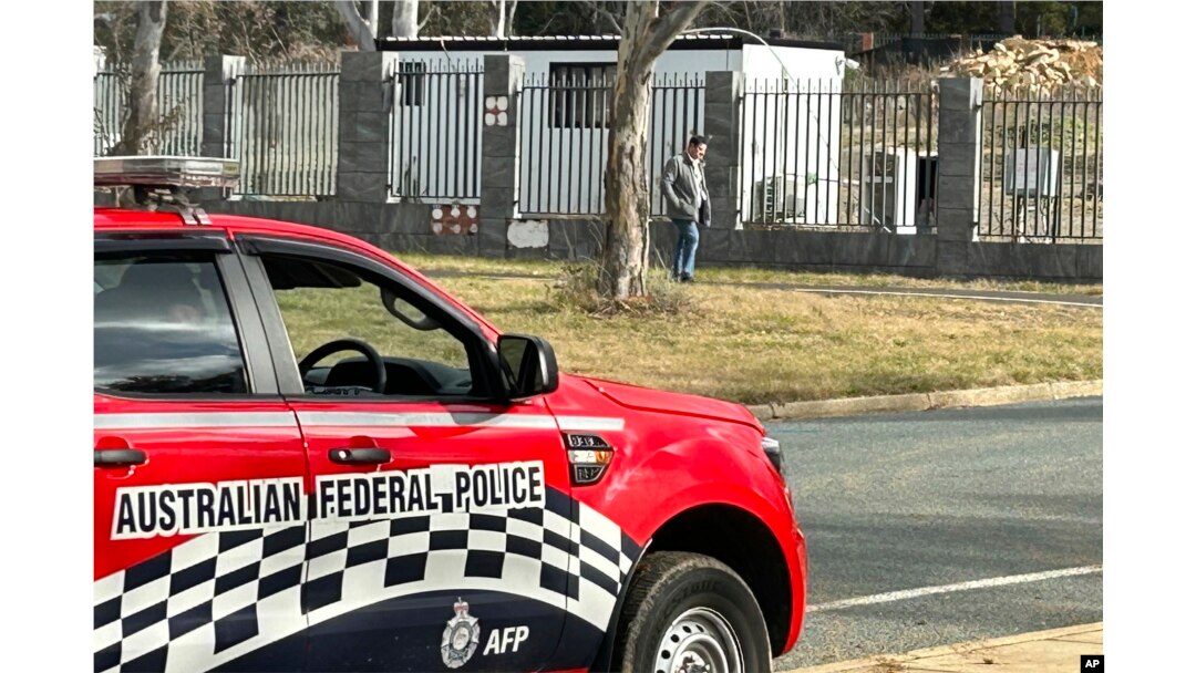 A man walks along a fence that surrounds a a building on the grounds of a proposed new Russian embassy near the Australian Parliament in Canberra where an Australian Federal Police officer observes from his vehicle, June 23, 2023.