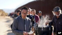 资料照片：2023年10月24日，在加利福尼亚州雅库姆巴附近，一名来自中国的男子在与其他人一起等待处理庇护申请时，从一名志愿者手中接过一碗燕麦粥。