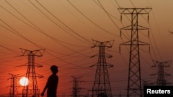 FILE - A local walks past electricity pylons during frequent power outages from South African utility Eskom, in Orlando, Soweto, South Africa, Sept. 28, 2022.