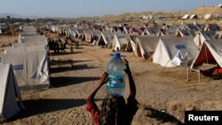 FILE - A girl carries a bottle of water she filled from nearby standing flood-waters at a camp for those displaced by recent flooding, in Sehwan, Pakistan, Sept. 30, 2022. 