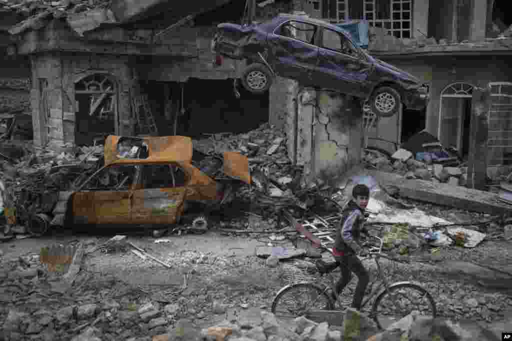 A boy rides his bike past destroyed cars and houses in a neighborhood recently liberated by Iraqi security forces, on the western side of Mosul.