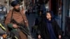FILE - A Taliban fighter stands guard as a woman walks past in Kabul, Afghanistan, Dec. 26, 2022. 