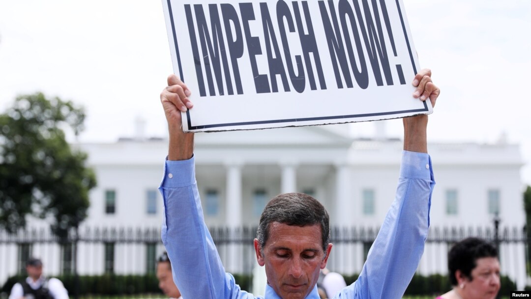 Steve Swanson protests in silence with a sign over his head reading “Impeach Now!” in front of the White House.