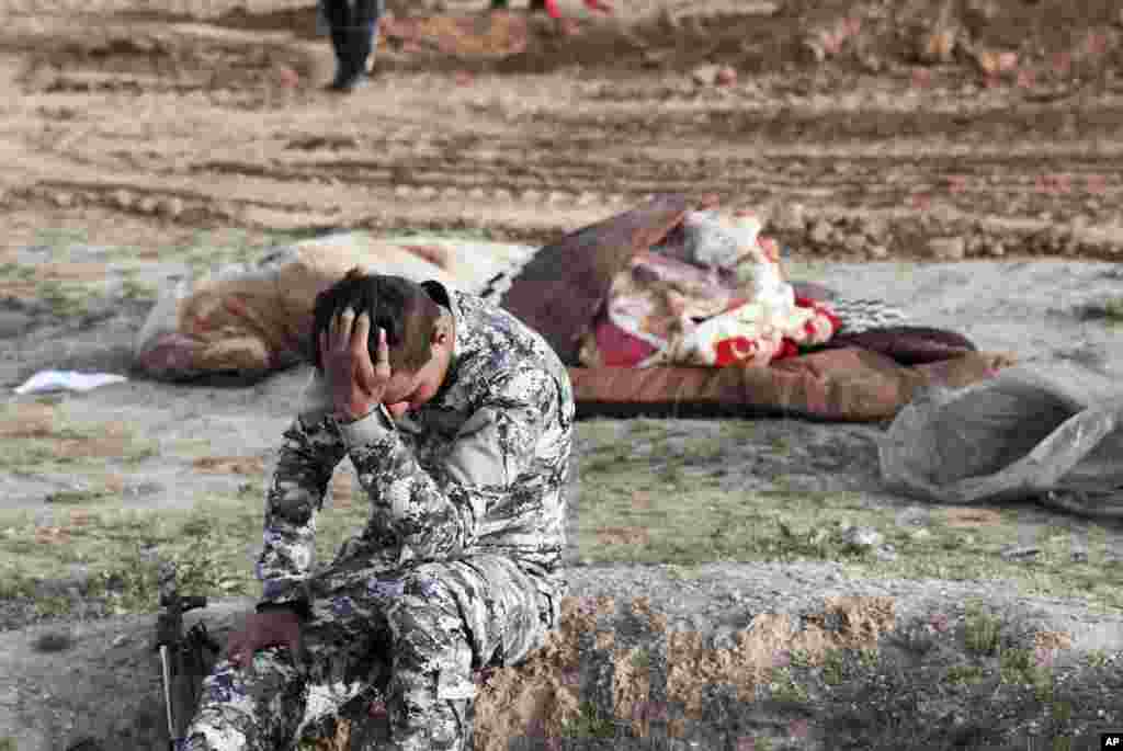 An Iraqi policeman pulls himself together as he is surrounded by bodies at the site of a mass grave containing some two dozen people, many of them children, in an area recently re-taken from Islamic State militants in Mosul, March 15, 2017.