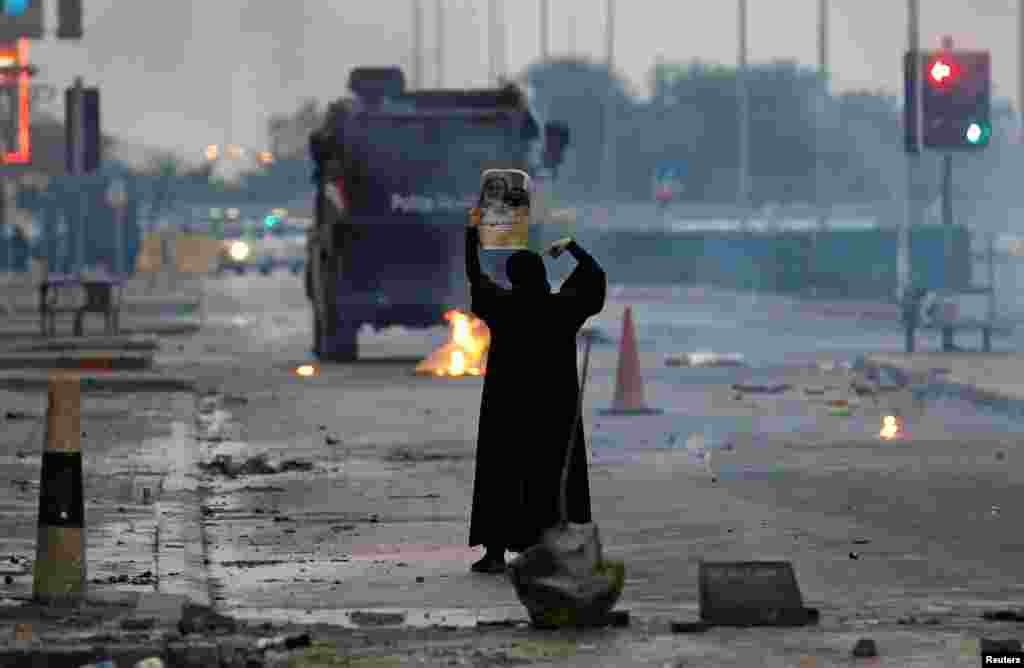 A female protester holds a photo of Shi'ite scholar Isa Qassim as she confronts riot police armored personnel carrier during a demonstration to mark the 6th anniversary of the February 14 uprising, in the village of Sitra, south of Manama, Bahrain.