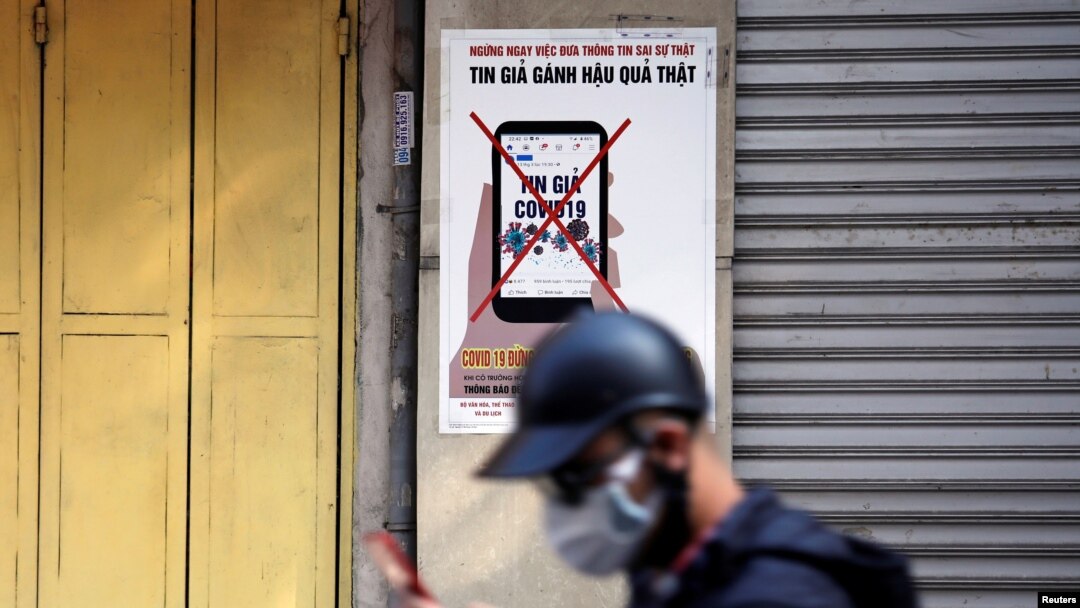 FILE - A man uses a smartphone as he walks past a poster warning against the spread of 'fake news' on the coronavirus, in Hanoi, Vietnam, April 14, 2020. Observers are seeing a crackdown on free speech ahead of a ruling party congress.