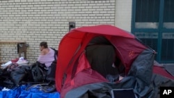 FILE: A person sits behind a tent on a sidewalk in San Francisco, Aug. 29, 2024.
