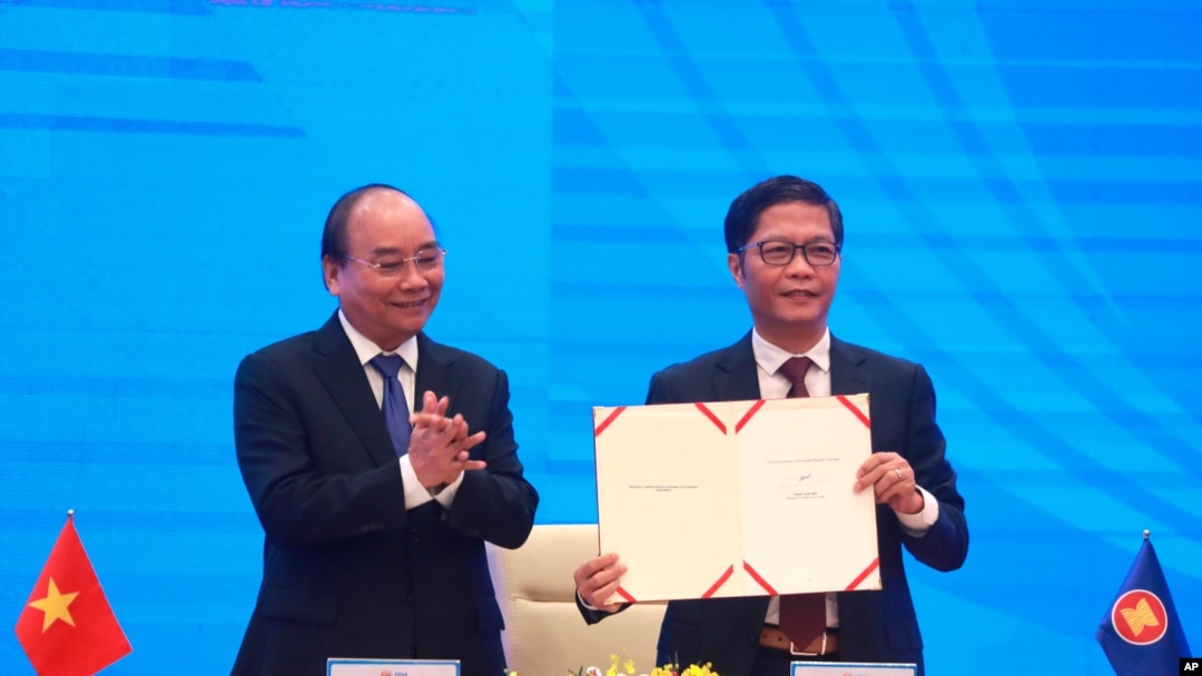 Vietnamese Prime Minister Nguyen Xuan Phuc, left, applauds as Minister of Trade Tran Tuan Anh holds a signed document during a virtual signing ceremony of the Regional Comprehensive Economic Partnership trade deal in Hanoi, Vietnam, Nov. 15, 2020.
