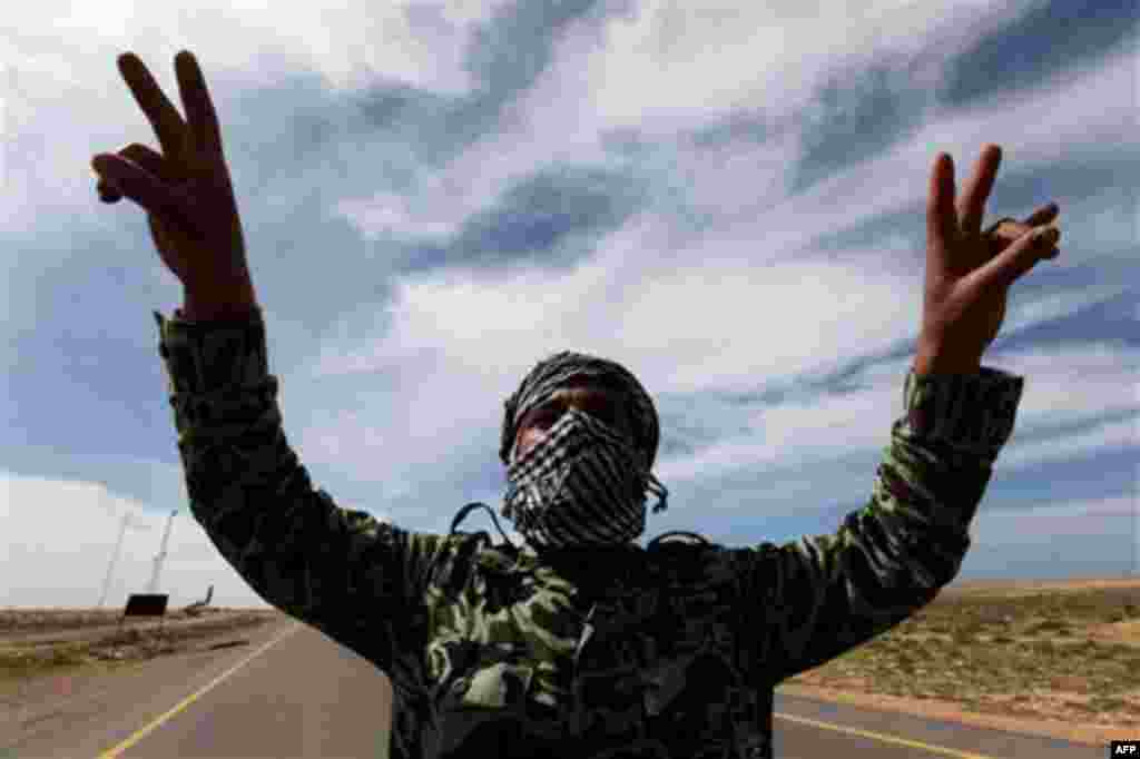 Anti-Libyan Leader Moammar Gadhafi rebel, flashes V signs at a desert road between Agela and Ras Lanouf towns, eastern Libya, Saturday March 12, 2011. An emergency European Union summit on Libya brought a no-fly zone no closer, but leaders embraced a new