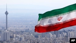 FILE - Iran's national flag flutters in the wind as the Milad telecommunications tower and buildings are seen in the background, Tehran, Iran, March 31, 2020. 