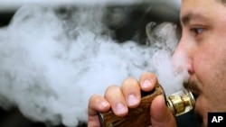 FILE - A man breathes vape from an e-cigarette at a vape shop in London, Aug. 17, 2018.