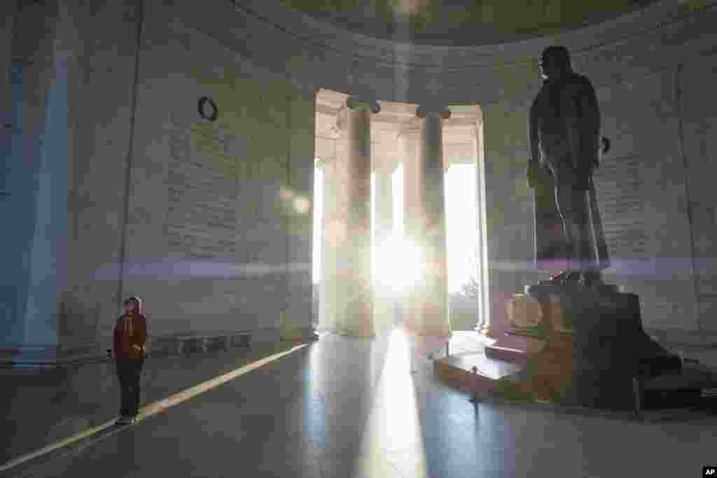 A tourist reads the inscriptions carved on the walls of the Jefferson Memorial as the early morning sun flares through the columns during the Presidents Day holiday in Washington, D.C.