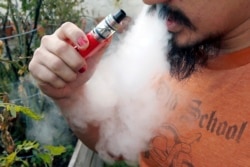 FILE - A man blows a puff of smoke as he vapes with an electronic cigarette, Oct. 18, 2019.