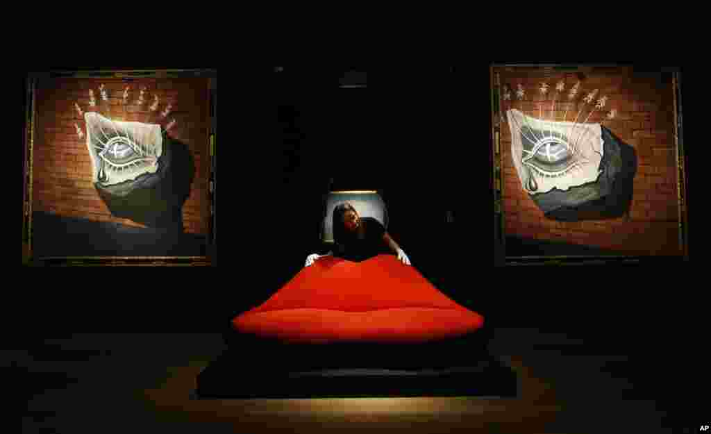 A Christie's employee adjusts a sofa called 'Mae West Lips Sofa' made by Salvador Dali and Edward James, in front of Salvador Dali's paintings 'L'oiel fleuri, decor pour le ballet Trist' at Christie's in London. The paintings and the sofa belong to a sale set for Tuesday.
