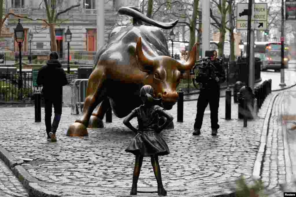 A photographer films a statue of a girl facing a statue of the Wall Street bull in the financial district in New York, March 7, 2017. The statue was installed by investment firm State Street Global Advisors. An inscription at the base reads, "Know the power of women in leadership. She makes a difference."