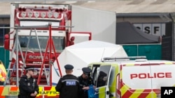 Police officers are on the scene after a truck, in rear, was found to contain a 39 dead bodies, later found to be Chinese nationals, in Thurrock, England, Oct. 23, 2019. 