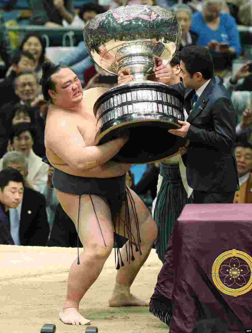 Japanese "yokozuna" or sumo grand champion Kisenosato (L) receives the championship trophy following his victory in the Spring Grand Sumo Tournament in Osaka, March 26, 2017.