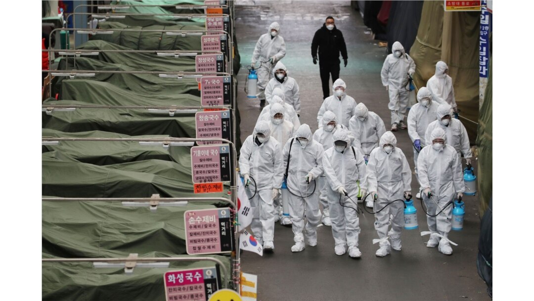 Workers wearing protective gear spray disinfectant at a market in the southeastern city of Daegu, South Korea, as a preventive measure after the COVID-19 coronavirus outbreak, Feb. 23, 2020.