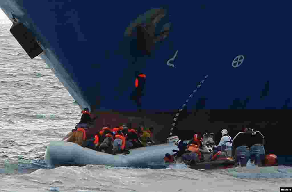 Migrants in a rubber dinghy fall into the sea alongside a rigid hulled inflatable boat of the Malta-based NGO Migrant Offshore Aid Station, as a migrant climbs onto the anchor of the Panama-registered ship Tuna 1 and one hangs onto its bow, after some 20 migrants on another rubber dinghy drowned in the central Mediterranean in international waters off the coast of Libya.