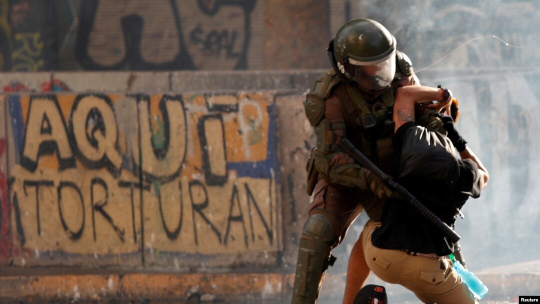 FILE - A police officer detains a demonstrator during a protest against Chile's government in Santiago, Chile, Nov. 5, 2019. The graffiti on the wall reads "Here they torture."