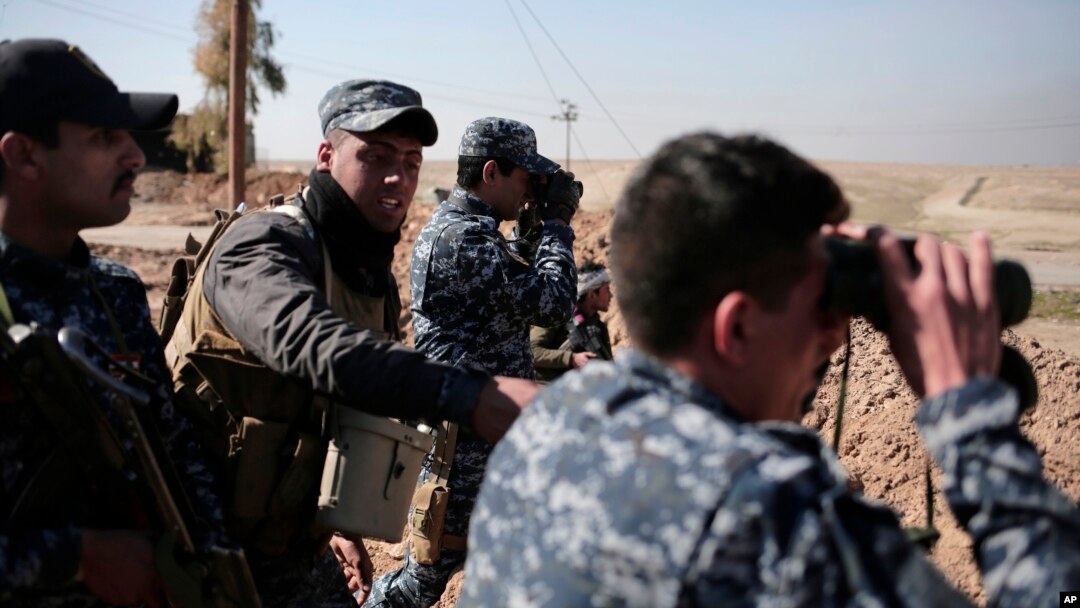 Iraqi federal police officers look towards Islamic State group territory as civilians flee the area, in the town of Albu Saif, Iraq, Feb. 21, 2017. A military spokesman says Iraqi forces are consolidating their gains south of Mosul ahead of moving deeper into the city's Islamic State-held western half.