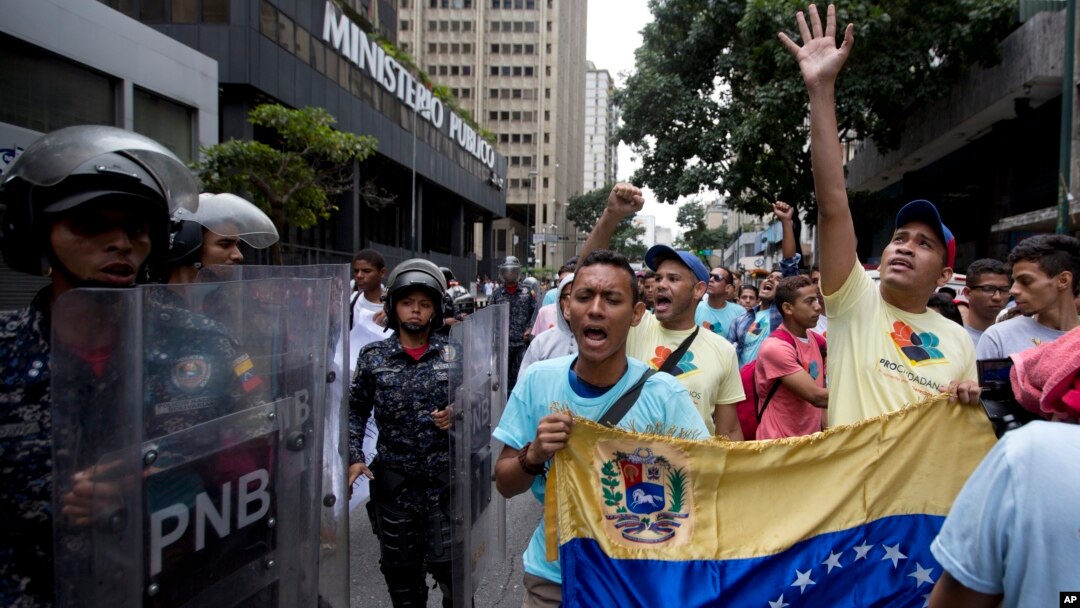 Opposition leader Leocenis Garcia, right, with members of his party, shout slogans against Venezuela's President Nicolas Maduro outside the attorney general's office, where police stand guard, in Caracas, Venezuela, July 18, 2018. The previous night, another opposition leader, Henrique Capriles, called on the country's political forces to reorganize in order to cope with the South American country's hyperinflation, and lack of food and medicine.