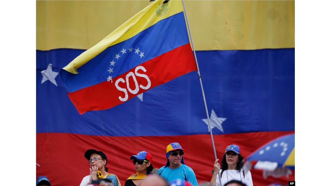FILE - A supporter of Venezuela's opposition leader and self-proclaimed interim president, Juan Guaidó, waves a Venezuelan flag marked with the letters "SOS" during a rally in Caracas, Venezuela, May 11, 2019.