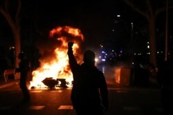 A protestors raises his fist at police across a burning barricade during clashes between protestors and police in Barcelona, Spain, Tuesday, Oct. 15, 2019.
