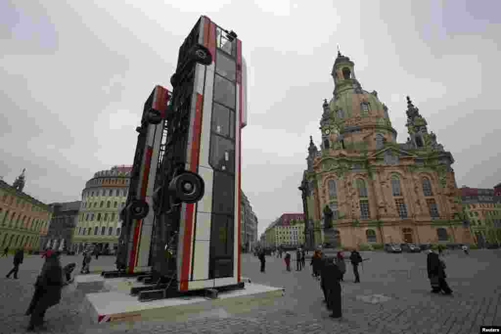 People walk next to the art installation "Monument" by Syrian artist Manaf Halbouni, made from three passenger buses, in Dresden, Germany.