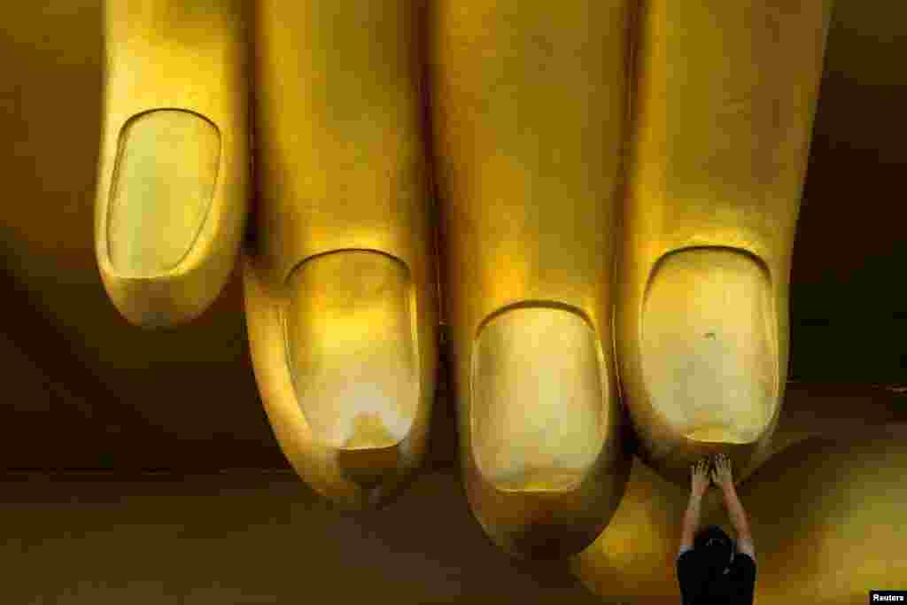 A woman touches the fingers of a Buddha statue and prays during the annual Makha Bucha Day, which celebrates Buddha's teachings, in Ang Thong, Thailand, Feb. 11, 2017.