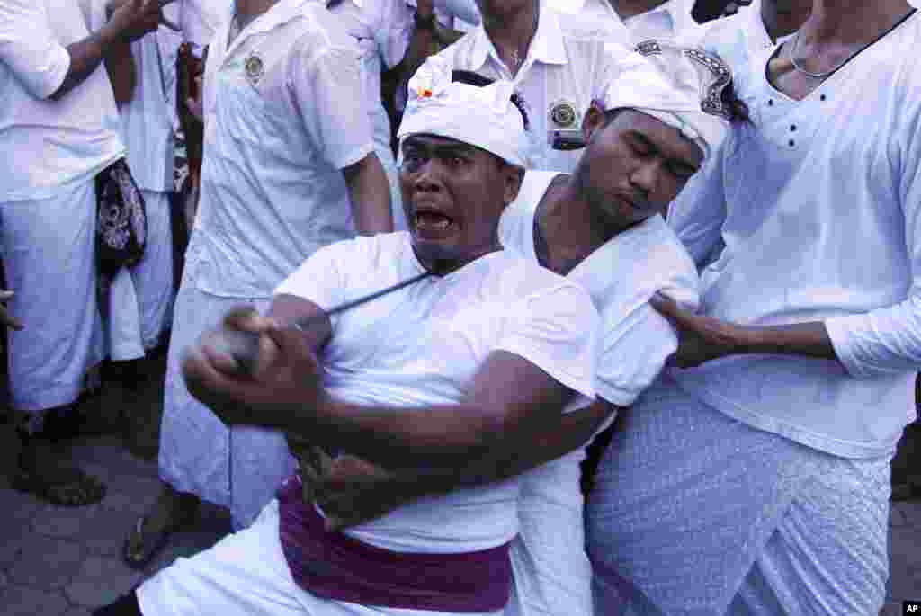 A man is placed into a trance like state with keris, traditional weapon, pointed to his neck during a hindu ritual called Ngerebong which is an ancient tradition of kesiman village, Bali, Indonesia.