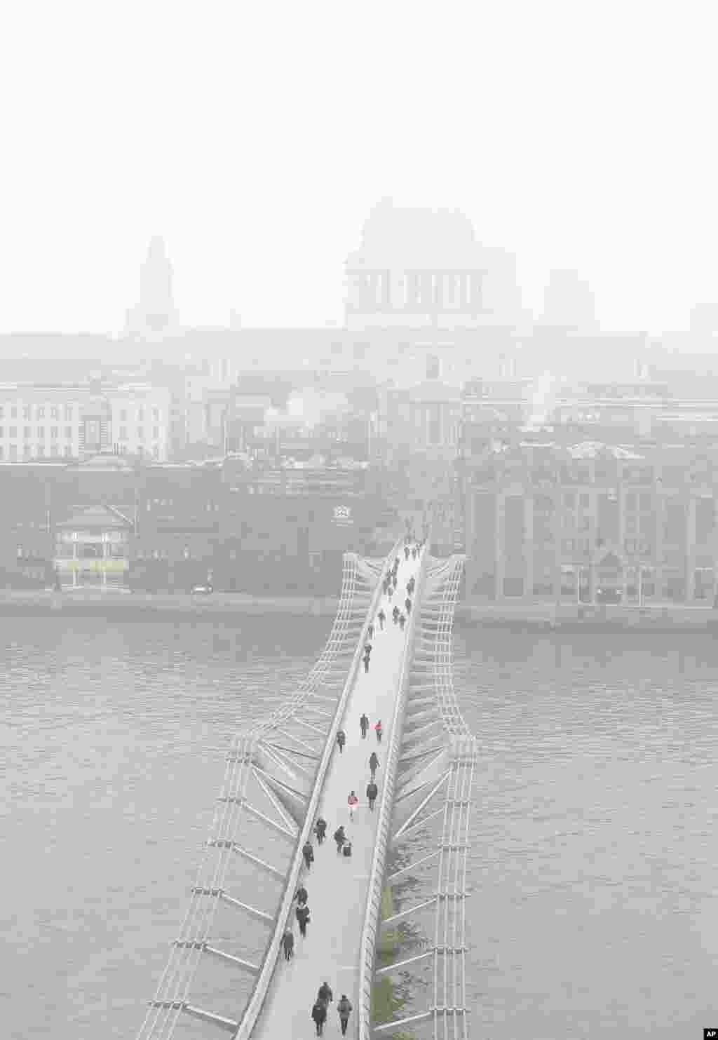 Pedestrians walk over the Millennium Bridge as fog shrouds St Paul's Cathedral in London.