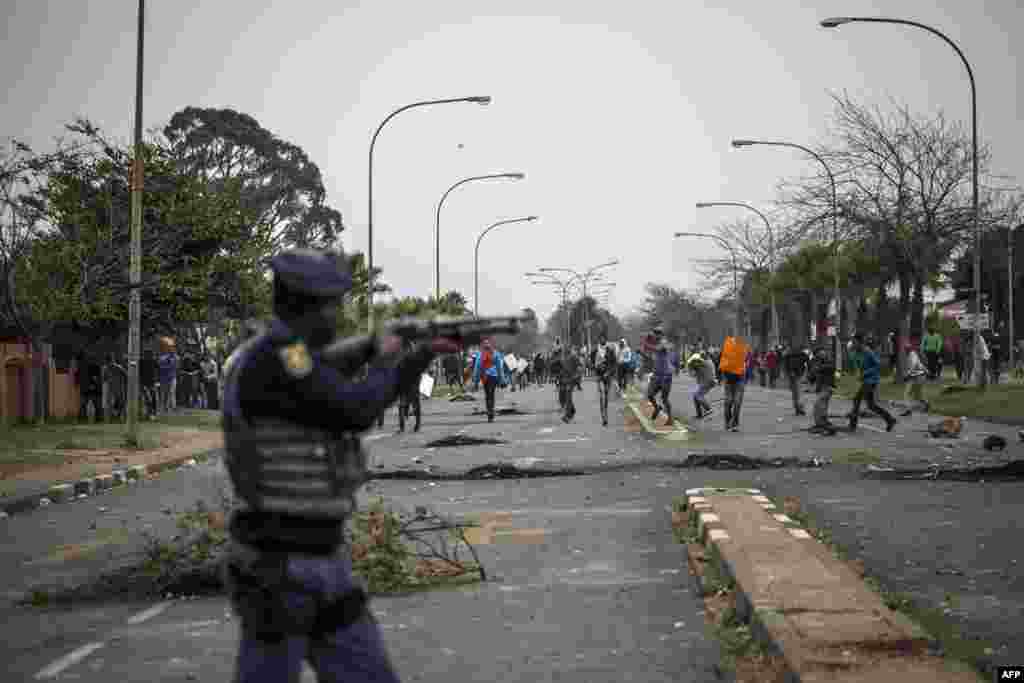 A South African riot police officer takes position as demonstrators protest against land grabbing, housing and unemployment, in the Eldorado Park and Freedom Park districts in Johannesburg, South Africa.
