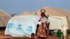 A woman walks past a child playing with water in a refugee camp in Sevare, Mali, Jan. 26, 2013. 