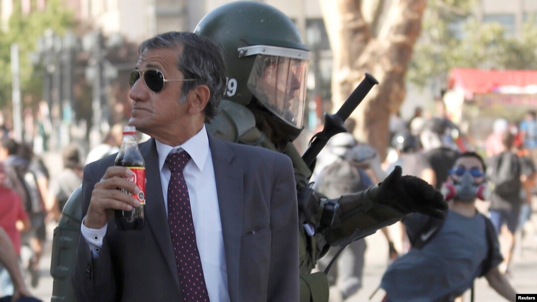 FILE - A man drinks a Frucola as a police officer chases demonstrators during a protest against Chile's government in Santiago, Chile, Dec. 4, 2019. 