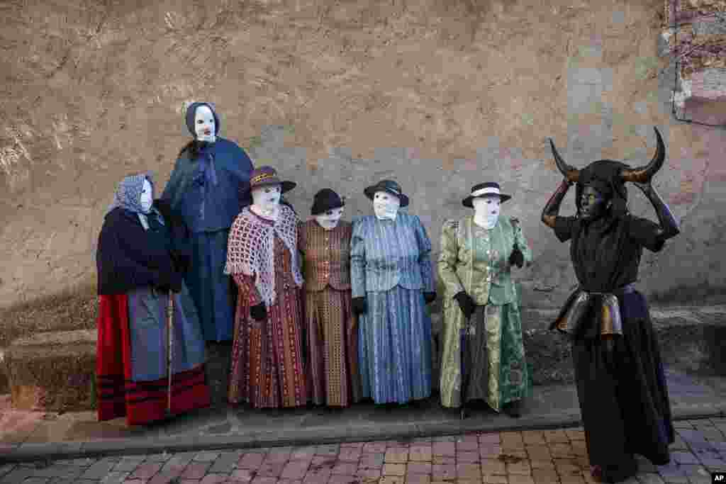 A reveler, dressed as "Diablos de Luzon" or Luzon Devil's, covered in oil and soot carrying bull horns on his head and cowbells on a belt representing the devil, and others dressed as "Mascaritas" take part in the carnival celebration in the small village of Luzon, Spain, Feb. 25, 2017.