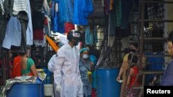 A worker wearing a 'Smart Helmet' thermoscanner that measures the temperature of people at a distance, screens residents in a slum Mumbai, India, July 23, 2020.