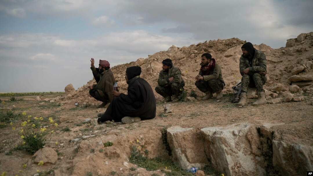 FILE - U.S.-backed Syrian Democratic Forces (SDF) fighters sit atop a hill in the desert outside the village of Baghuz, Syria, Feb. 14, 2019.