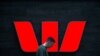 FILE - A pedestrian looks at his phone as he walks past a logo for Australia's Westpac Banking Corp outside a branch in central Sydney, Nov. 5, 2018.