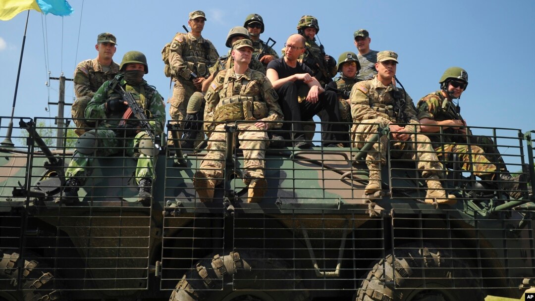 Ukraine's Prime Minister Arseniy Yatsenyuk, center, surrounded by U.S. and Ukrainian soldiers atop an armored personnel carrier in Lviv region, western Ukraine, June 3, 2015.