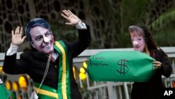 Demonstrators wear masks of Brazil's President Jair Bolsonaro, left, and Germany's Chancellor Angela Merkel during a protest in defense of the Amazon in Rio de Janeiro, Brazil, Sept. 5, 2019. Germany has suspended a line of funding for Amazon projects.