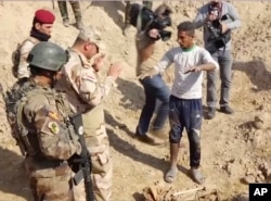 Iraqi security forces speak to shepherd Khalaf Luhaibi next to bones on the ground at an abandoned base near the northern town of Hawija, Iraq, Nov. 22, 2017.