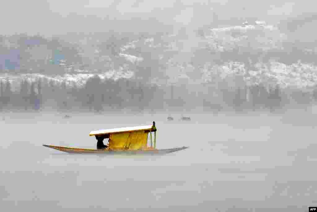 Kashmiri boatmen paddle a shikara across Dal Lake amid dense fog following rainfall in Srinagar, India.