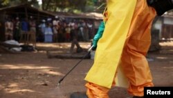 FILE - A member of the French Red Cross disinfects the area around a motionless person suspected of carrying the Ebola virus as a crowd gathers in Forecariah, Guinea, Jan. 30, 2015.