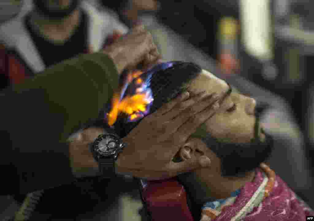 Barber Ramadan Edwan performs a technique that utilizes fire to straighten his client's hair, in the Rafah refugee camp, in the southern Gaza Strip.