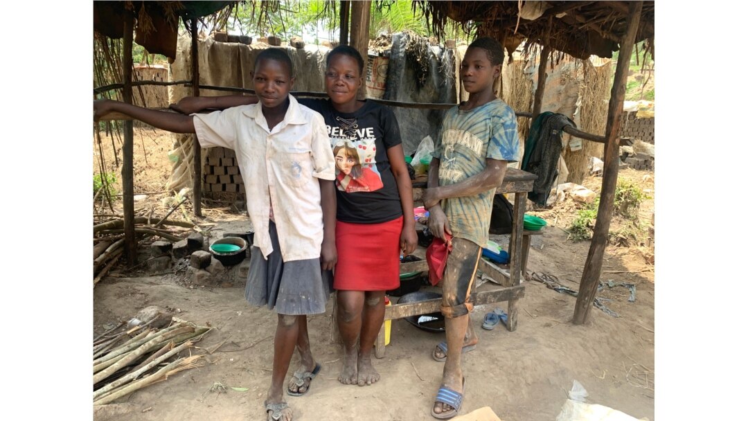 Nayigga Rashidah stands with two of her children in front of their makeshift restaurant in Ntawo village, Mukono district Uganda, Aug. 1, 2020. (Halima Athumani/VOA)