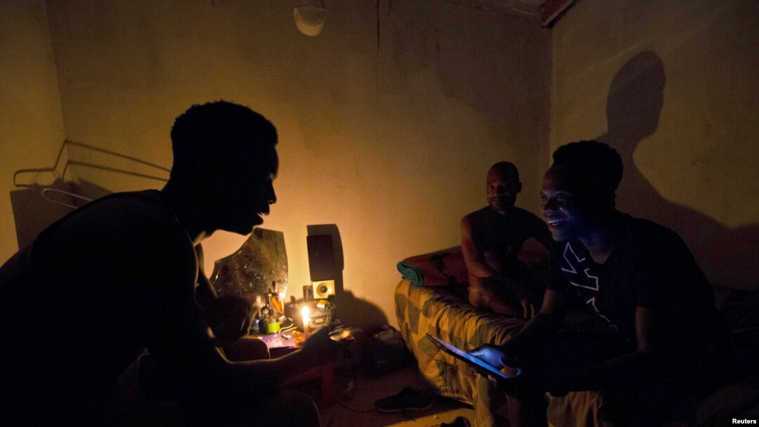 FILE - Friends talk by candlelight during load shedding in Embo, South Africa, March 18, 2019. 