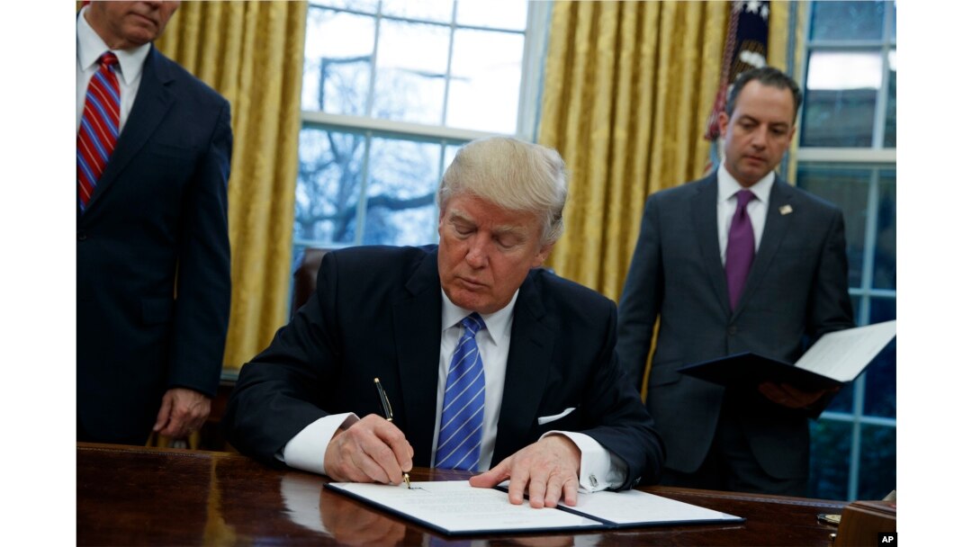 FILE - President Donald Trump signs an executive order to withdraw the U.S. from the 12-nation Trans-Pacific Partnership trade pact agreed to under the Obama administration, Jan. 23, 2017, in the Oval Office of the White House.