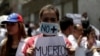 A woman wears a mask and a banner that read "No more deaths" as she takes part in a rally of workers of the health sector against President Nicolas Maduro's government in Caracas, Venezuela, May 17, 2017. 